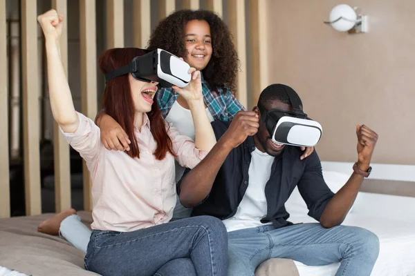 Happy multiracial family having fun on weekend, watching movie and playing game in virtual reality glasses, celebrating success, clenching fists and screaming Stock Image