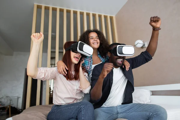 Realitas yang tidak nyata. Terkejut keluarga yang baik mengangkat tangan saat mencoba kacamata VR dan beristirahat pada yang buruk. Keluarga multirasial bersukacita di rumah. Konsep teknologi. Stok Gambar