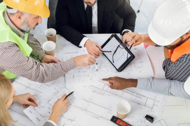 Ofisteki planları analiz eden çok kültürlü meslektaşlar, inşaatçılar veya mimarlar