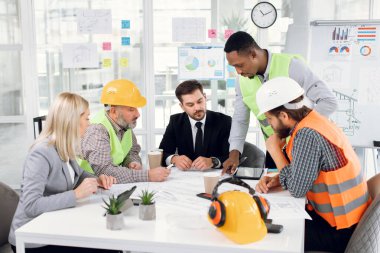 Modern ışık ofisinde çizim denetimiyle çalışan çok kültürlü ortaklar.