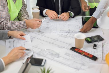 Mimarlar, mühendisler ve tasarımcılar planları analiz eder, masada otururlar.
