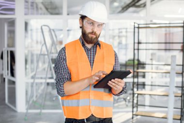 Kasklı ve gözlüklü sakallı mühendis tablet üzerinde çalışıyor.