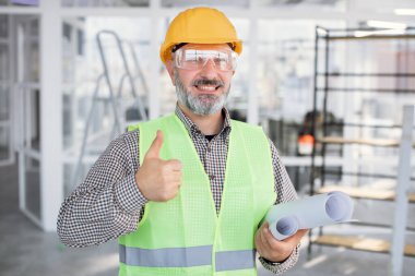 Gözlüklü ve miğferli gülümseyen sakallı adam başparmağını kaldırıyor.