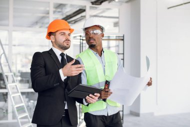 Kafkas ve Afrikalı erkek mühendisler inşaat sahasında proje üzerinde çalışıyorlar.