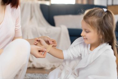 Genç bir kadının evdeki küçük bir kızın koluna sıva sürerken çekilmiş görüntüsü. Annesi yara bandı yapıştırırken küçük tatlı bir kız koluna bakıyor.