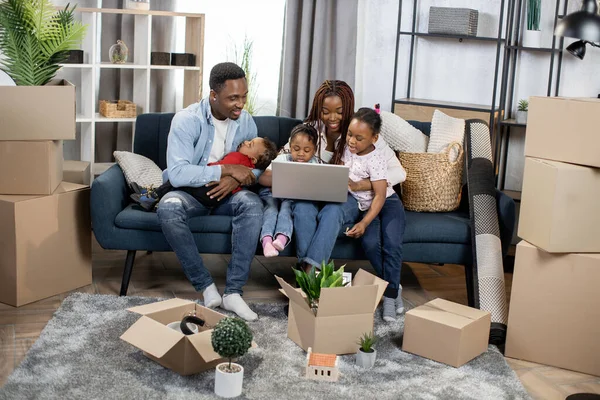 Parents with kids sitting at new flat with boxes and laptop