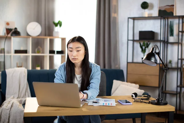 Asian woman sitting at desk and typing on laptop