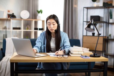Video çağrısı için kulaklık ve laptop kullanan Asyalı kadın.