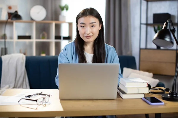 Beautiful asian woman working on laptop, sitting at the table in light living room interior