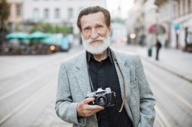 Yaşlı adam dışarıda beklerken eski fotoğraf makinesini tutuyor.