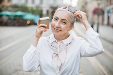 Gülümseyen son sınıf öğrencisi bir fincan kahveyle sokakta duruyor.