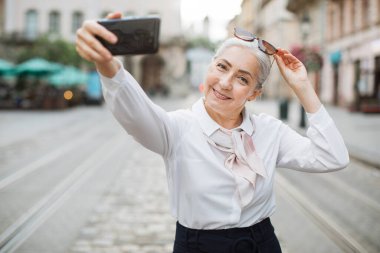 Kadın emekli, selfie çekmek için akıllı telefon kullanıyor.