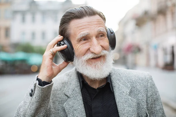 Positive senior man listening music in headphones outdoors