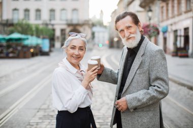 Yaşlı çift sokakta bir kutu kahveyle kadeh kaldırıyor.