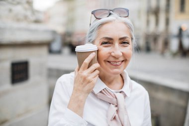 Kadın emekli dışarıda oturuyor ve kahve içiyor.