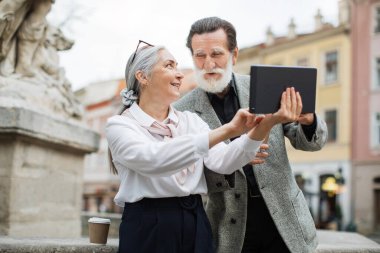 Tabletli yaşlı adam ve kadın sokakta kahve içiyorlar.