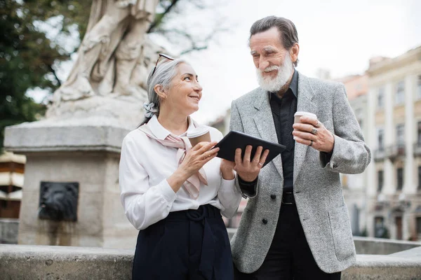 Mutlu yaşlı çift tablet kullanıyor ve dışarıda kahve içiyor.