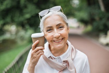 Parkta elinde kahveyle bekleyen çekici, yaşlı bayan.