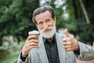 Son sınıf öğrencisi elinde bir fincan kahveyle başparmağını kaldırıyor.