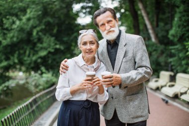Kafkasyalı yaşlı çift parkta kahve fincanlarıyla bekliyor.