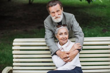 Kıdemli adam parkta güzel karısına nazikçe sarılıyor.