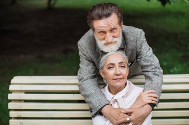 Kıdemli adam parkta güzel karısına nazikçe sarılıyor.