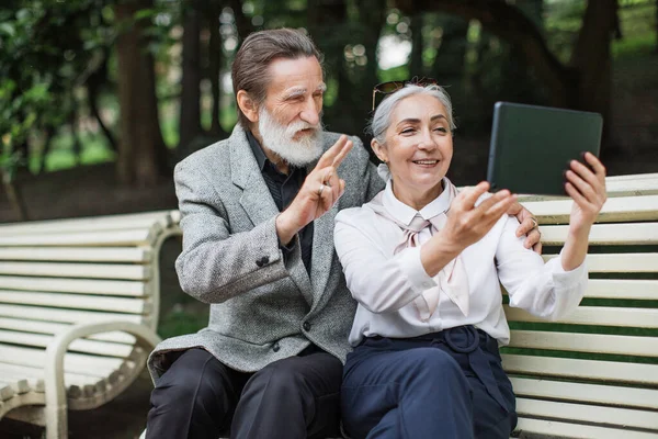 Cheerful mature couple using tablet for video chat outdoors