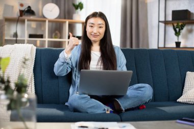 Kanepede dizüstü bilgisayarıyla oturan ve parmağını gösteren bir kadın.