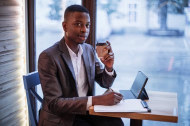 Afrikalı adam kahve içiyor ve kafede tablet kullanıyor.