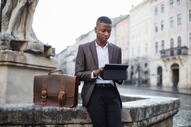 Dışarıda tablet kullanan takım elbiseli genç bir zenci.