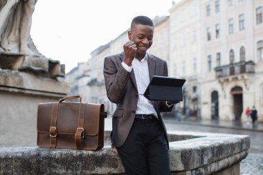 Gülümseyen Afrikalı işadamı sokakta tablet üzerinde çalışıyor.