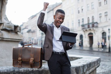 Gülümseyen Afrikalı işadamı sokakta tablet üzerinde çalışıyor.
