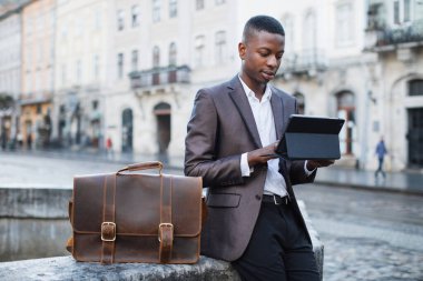 Dışarıda tablet kullanan takım elbiseli genç bir zenci.