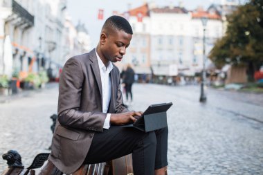 Bankta oturup tablet üzerinde çalışan odaklanmış siyah bir adam.