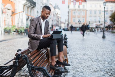 Bankta oturup tablet üzerinde çalışan odaklanmış siyah bir adam.