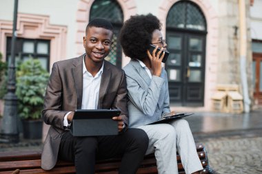 Adam tablet kullanırken Afro kadın cep telefonundan konuşuyor.
