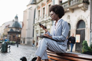 Cep telefonu kullanan ve panoya yazı yazan Afro iş kadını