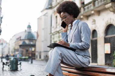 Siyah kadın cep telefonundan konuşuyor ve panoya yazı yazıyor.