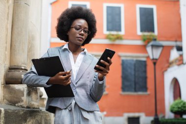 Zenci iş kadını sokakta akıllı telefon kullanıyor.