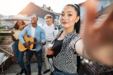 Arkadaşlar gitar çalarken bir kadın selfie çekiyor.