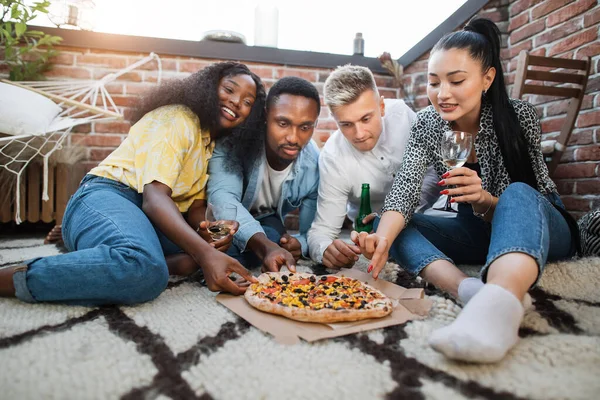 Dört arkadaş içki içiyor ve çatıda pizza yiyor. — Stok fotoğraf