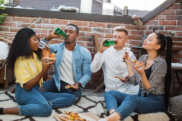 Quatre personnes multiculturelles buvant de l'alcool et mangeant des pizzas — Photo