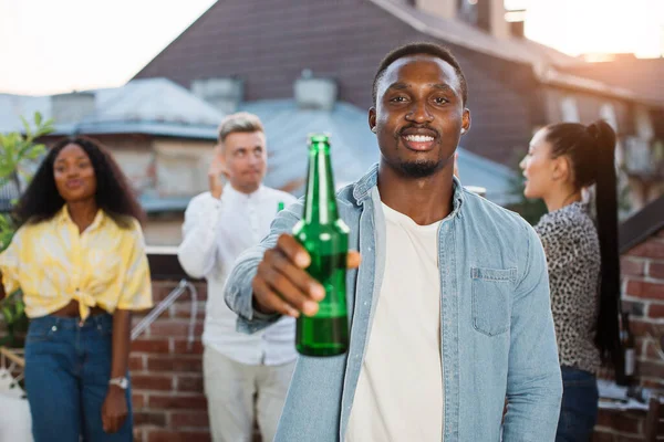 Afro homme posant avec de la bière tandis que des amis dansent derrière — Photo