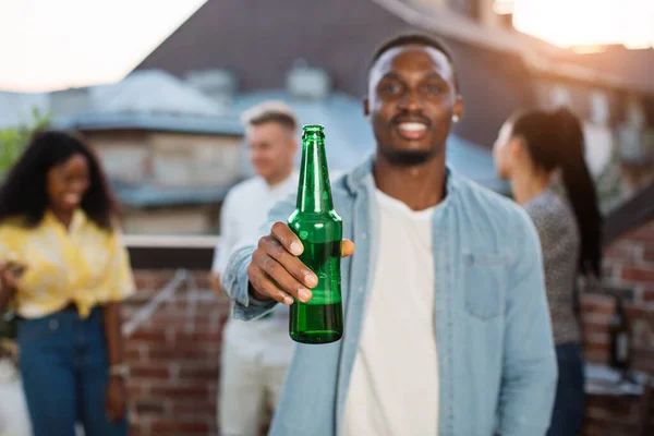Afro homme posant avec de la bière tandis que des amis dansent derrière — Photo
