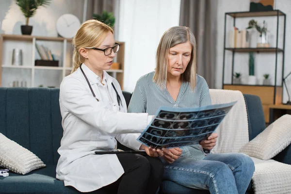 医生和老年妇女在家访时正在看X光扫描图像。老太太一边听女医生解释CT扫描，一边谈论治疗 — 图库照片