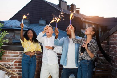 Dört arkadaş çatıda havai fişeklerle kutlama yapıyor.
