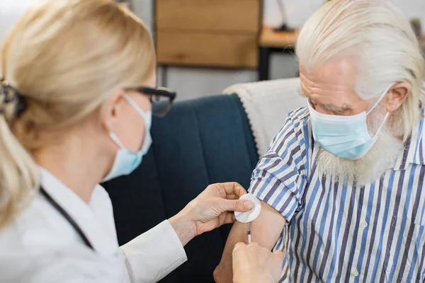 Vaccination, insulin injection. High-skilled professional female doctor doing injection of insulin to elderly bearded diabetic man during visiting him at home
