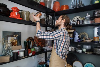 Sakallı adam tabletle dükkan çeşitlerini kontrol ediyor.