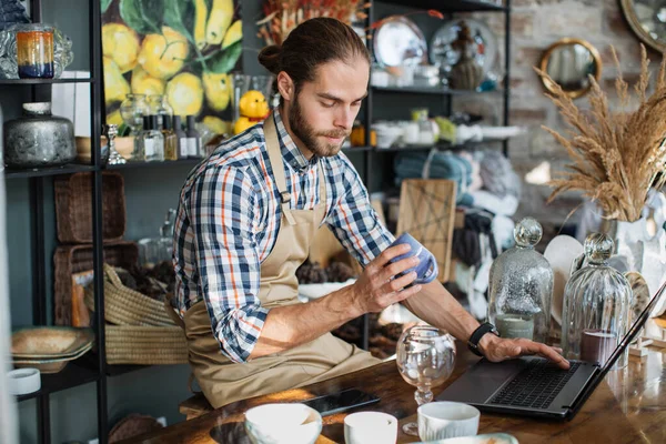 Hombre caucásico usando el ordenador portátil para contar bienes en la tienda de decoración —  Fotos de Stock