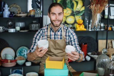 Gülümseyen sakallı adam dekor dükkanında tezgahta oturuyor.